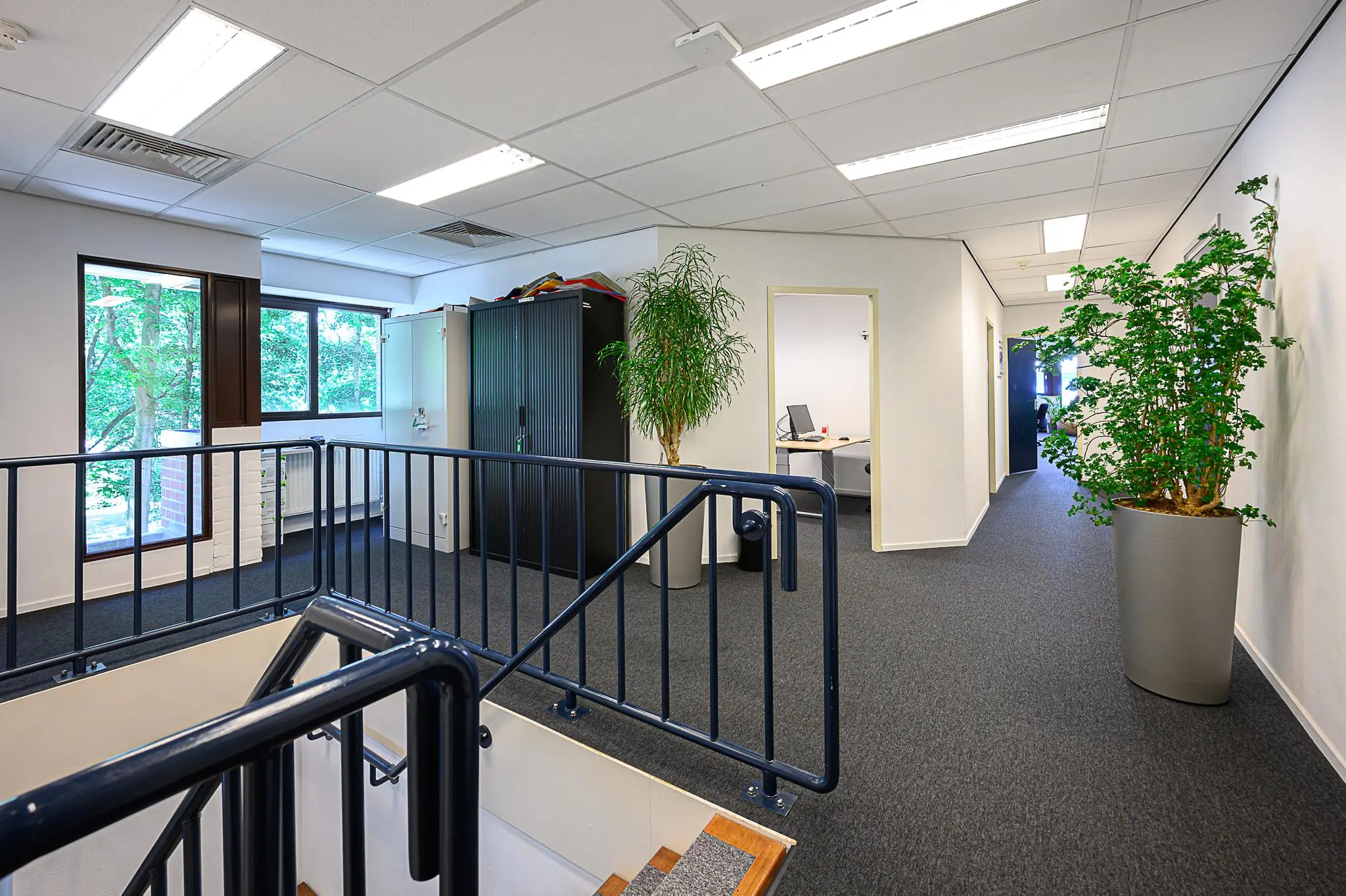 Moderne kantoorruimte met bureaus, kasten, planten en een trapleuning in gebouw De Linie.